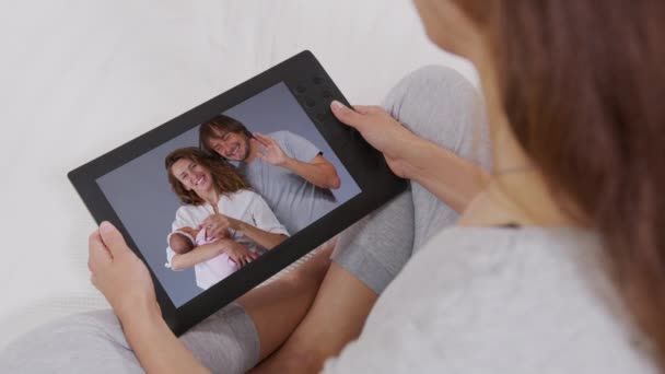 Pandangan belakang wanita muda, bersantai di sofa sambil berbicara dengan anak-anak dan cucu-cucunya menggunakan tablet digital di rumah. Keluarga bahagia. chatting online. — Stok Video
