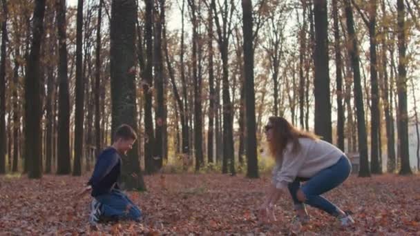 Femme avec feuille et son enfant garçon faisant des feuilles se battent dans la cour d'automne. — Video