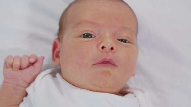 Nahaufnahme des Gesichts eines Neugeborenen in den ersten Tagen, das aufwacht und seine Augen öffnet. Ein neugeborenes Baby Grimassen durch einen Traum. Neugeborenes in den ersten Minuten des Lebens. — Stockvideo