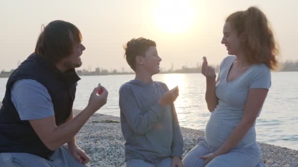 Повільний рух щасливих батьків з крекерами на узбережжі на заході сонця. Сімейне святкування . — стокове відео
