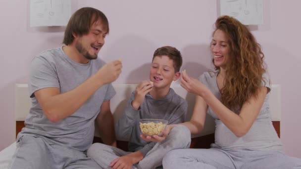 Glückliche Familie erwachsene Eltern Mama Papa und süße kleine Junge fernsehen zusammen essen Snack genießen Fernsehen zusammen Lounge auf dem Sofa Spaß im Wohnzimmer zu Hause — Stockvideo