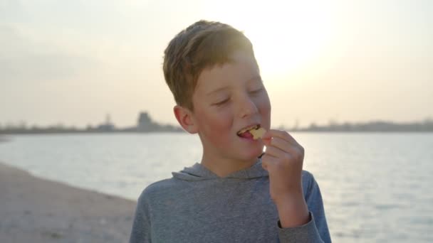 Mouvement lent du garçon heureux avec des craquelins sur la côte au coucher du soleil. Célébration familiale. — Video