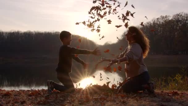 葉を持つ女性と子供の男の子は秋の庭で戦います. — ストック動画