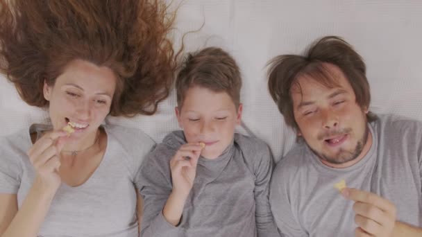 Felice famiglia genitori adulti mamma papà e carino bambino guardando la tv insieme mangiare spuntino godere di televisione insieme lounge sul divano divertirsi in soggiorno a casa. — Video Stock