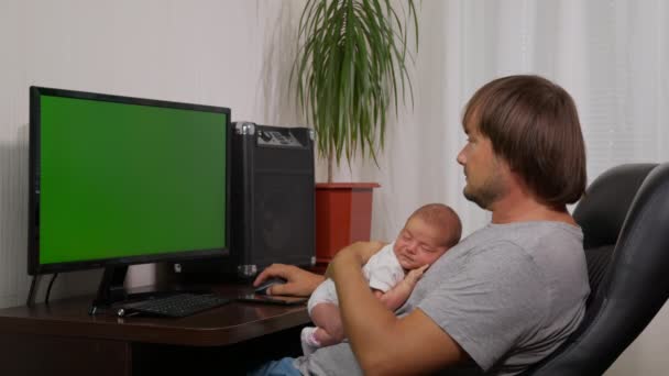 Un joven hombre de negocios con un bebé en sus brazos trabaja en casa en la computadora. Pantalla verde . — Vídeos de Stock