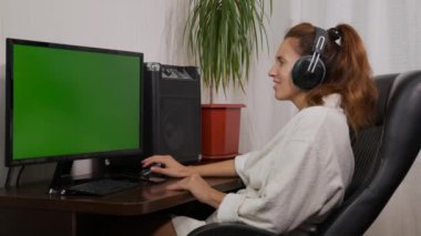 Bir kadın yeşil ekranlı televizyon izliyor ve kulaklıkla müzik dinliyor..