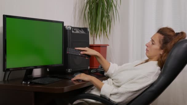 Μια γυναίκα βλέπει τηλεόραση με πράσινη οθόνη. Εναλλαγή καναλιών με το τηλεχειριστήριο. — Αρχείο Βίντεο