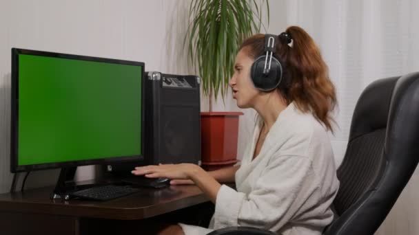 Žena se dívá na televizi se zelenou obrazovkou a poslouchá hudbu na sluchátkách. — Stock video