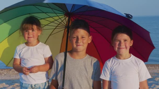 Glückliche Kinder, die sich mit Sonnenschirm am Strand drehen. Regenbogenschirm. Sonniger Tag. — Stockvideo