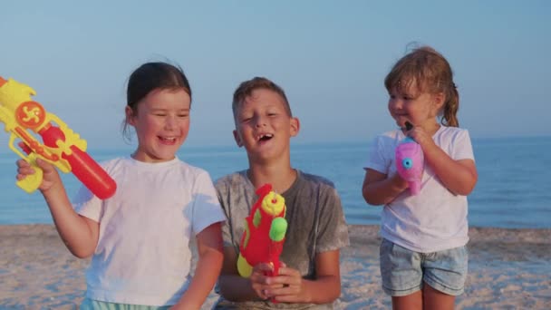 Маленькі дівчатка і хлопчик на морі. Діти грають з водяними гарматами . — стокове відео