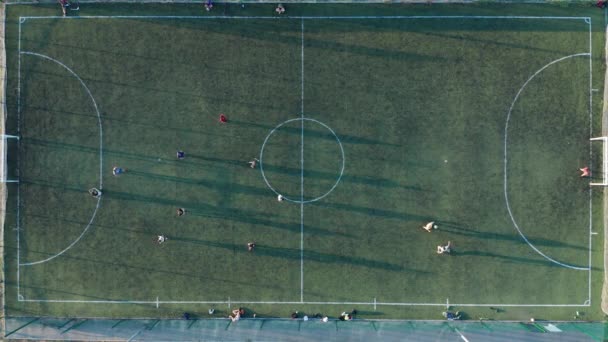 Αεροπλάνο Δύο ομάδες παίζουν μπάλα σε εξωτερικούς χώρους ποδοσφαίρου, κορυφαία θέα. Ποδόσφαιρο παιχνίδι σε εξωτερικούς χώρους, πράσινο πεδίο με σημάνσεις, παίκτες που τρέχουν γύρω με μια μπάλα. — Αρχείο Βίντεο