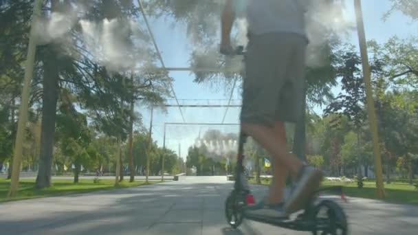 Boy rijdt scooter op de weg in het groene zomerpark. Kind leert scooters te berijden. Concept sport en gezondheid. — Stockvideo
