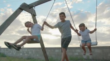 Çocuklar gün batımında salıncakta sallanıyor..