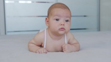 Güzel, gülümseyen bebek: Yatağa uzanmış güzel, küçük bir bebek kameraya gülümsüyor..