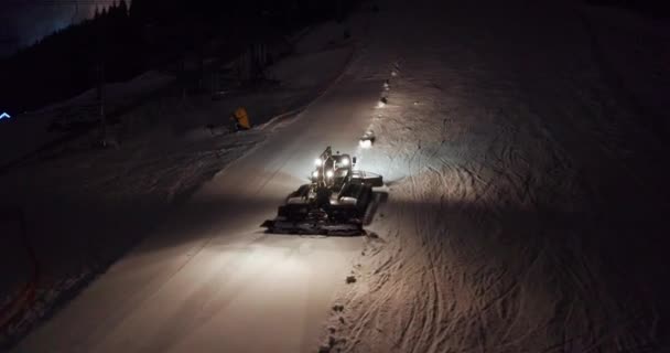 Letecký pohled. Snow Grooming Snowcat Machines Fix Trail on Ski Resort Slope at Night. — Stock video