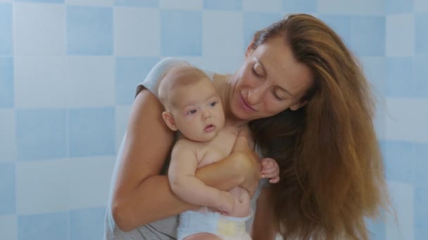 Liebevolle zarte junge Mutter hält entzückende süße Mädchen Tochter umarmt küssende kleine Kind. Glückliche liebevolle Mutter kuschelt mit Säugling und steht zu Hause. — Stockvideo