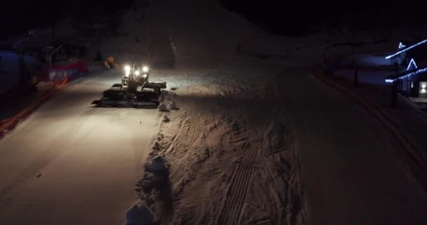 Luftaufnahme. Orange beleuchtete Schneekatze fährt in der abendlichen Dunkelheit mit aktiven Touristen den weißen schneebedeckten Hügel hinauf. — Stockvideo