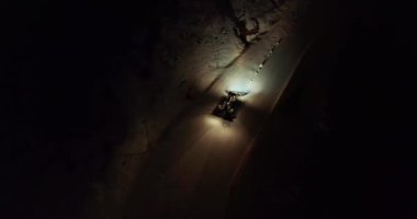 Turuncu ışıklı kar aracı, akşam karanlığında beyaz karlı tepe boyunca ilerliyor..