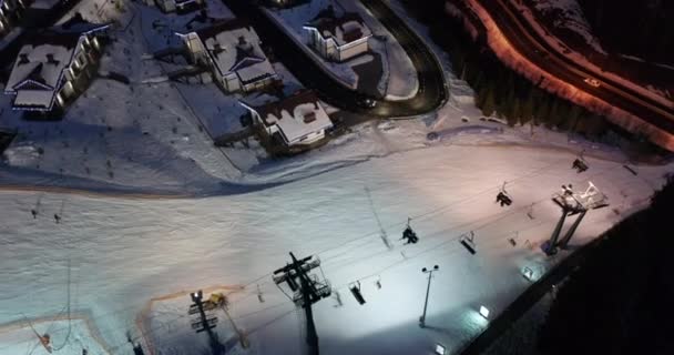 Vista aérea de los esquiadores bajan pistas de esquí cerca de remontes en la estación de esquí por la noche. — Vídeos de Stock