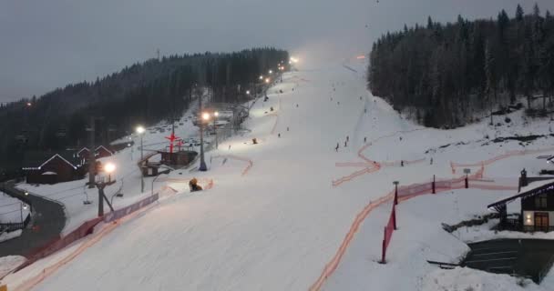 Vue aérienne des pistes de ski avec skieurs et remontées mécaniques sur la station de ski dans la forêt d'hiver contre les montagnes enneigées. Journée ensoleillée. Pistes de ski avec pins. Des collines des Carpates. Bukovel. — Video