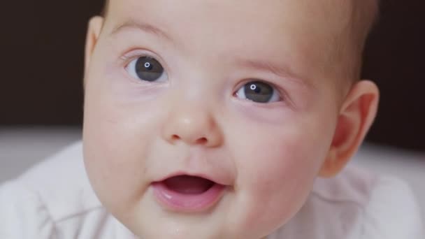 Belle Bébé Souriant : Un magnifique petit bébé se trouve sur le lit et sourit à la caméra avec un joli fond de mise au point douce. — Video
