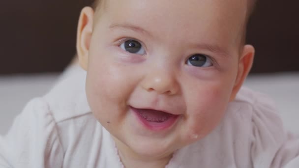 Belle Bébé Souriant : Un magnifique petit bébé se trouve sur le lit et sourit à la caméra avec un joli fond de mise au point douce. — Video