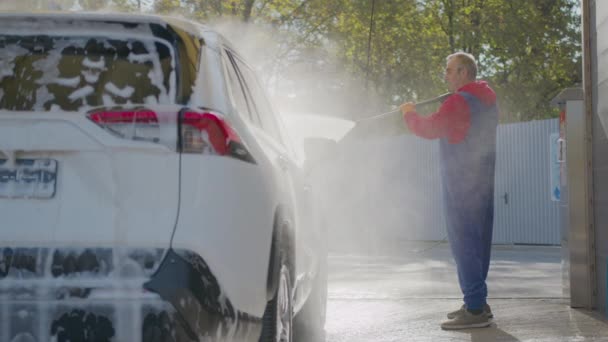 Starszy mężczyzna myje samochód pianką i wodą.. — Wideo stockowe