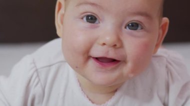 Küçük güzel kızın gülümsemesinin yavaş çekimini kapat. Bebek gülümsemesinin kapalı mekândaki portresi..