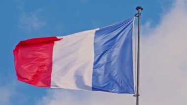 Flag France waving on a metal flagpole, against the background of light clouds on a sunny day.