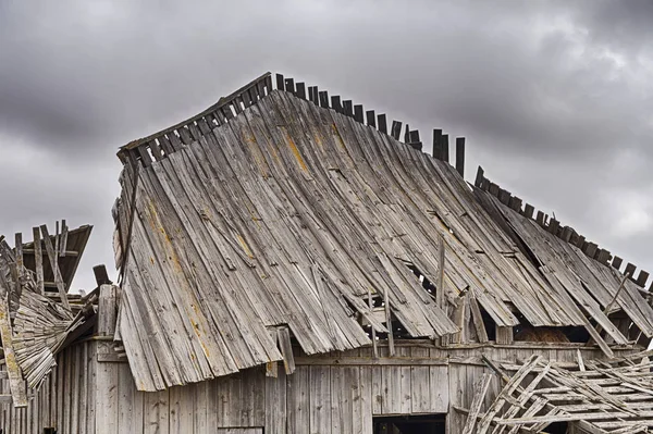 屋顶坍塌的老木谷仓的车顶是在一个戏剧性的多云天空中勾勒出来的 — 图库照片