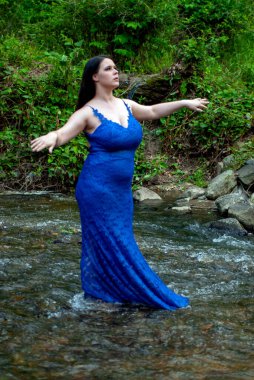 Nehirde mavi elbiseli, uzun saçlı güzel bir genç kız.