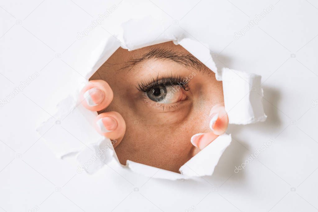young woman peeks through a hole in a paper white wall