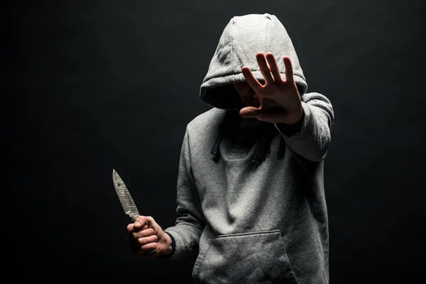 Dangerous man in the hood stands in the dark and holds a knife. The face is not visible. The concept of crime, murder.