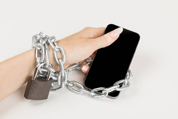 iron chain with the lock connects the female hand and the smartphone together. the concept of dependence on the mobile phone.