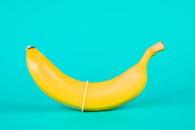 Mavi arka planda kondom ve muz yakın planda..