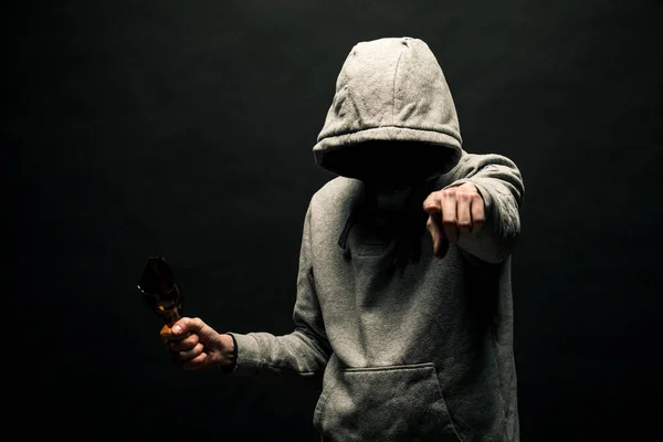 A dangerous hooded man stands in the dark and holds a broken bottle. The face is not visible. The concept of crime, murder.