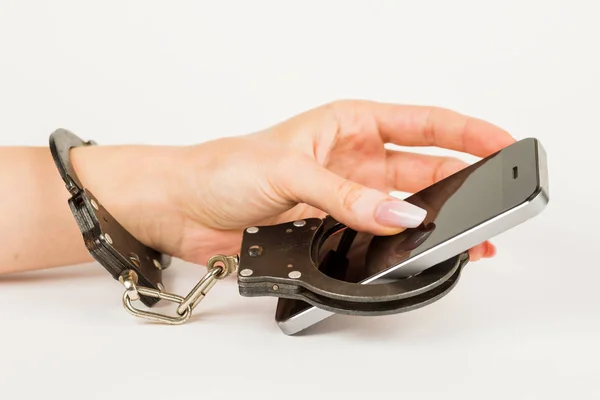 handcuffs connects the female hand and the smartphone together. the concept of dependence on mobile phone.