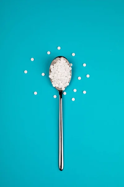 Sugar substitute pills in a spoon, on a blue background.