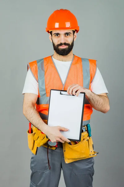 Ein Bauarbeiter Mit Orangefarbenem Helm Auf Grauem Hintergrund Signalisiert Etwas — Stockfoto