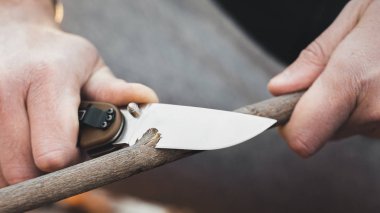 Turistin ellerinin yakın çekim, bir bıçak ile bir sopa bileme. Seyahat, aşırı ve hayatta kalma kavramı.