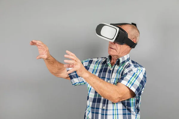 Grandfather looks into VR glasses, hand gestures, on a gray background