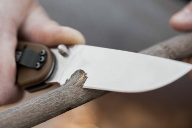 Turistin ellerinin yakın çekim, bir bıçak ile bir sopa bileme. Seyahat, aşırı ve hayatta kalma kavramı.