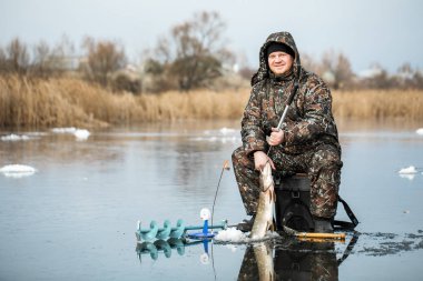 Genç bir adam bir delikten buzda balık tutuyor. Balık tutma kış.