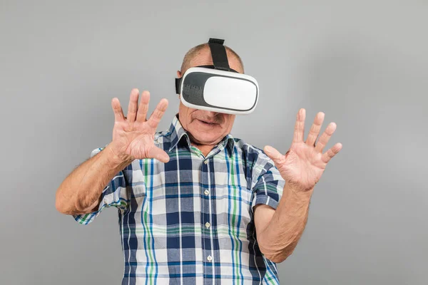 Grandfather looks into VR glasses, hand gestures, on a gray background