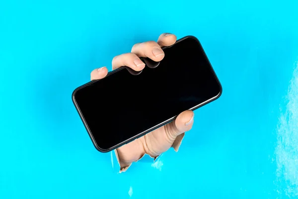 A woman holding a phone through a torn blue paper.