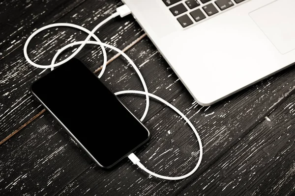 A USB cable connects your phone and laptop. On the black table