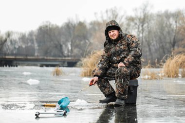 Genç bir adam bir delikten buzda balık tutuyor. Balık tutma kış.