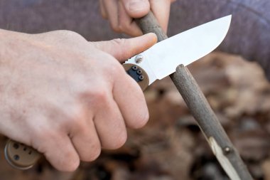 Turistin ellerinin yakın çekim, bir bıçak ile bir sopa bileme. Seyahat, aşırı ve hayatta kalma kavramı.