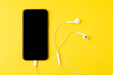 Sarı arka planda kulaklıklı akıllı telefon. Müzik dinleyin.