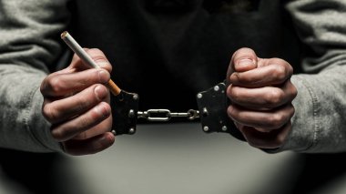 Bir uyuşturucu bağımlısı Sigara İçilmeyen ile kelepçeli tutuklandı. Koyu siyah arka plan bağımlılığı gri sweatshirt muzdarip.
